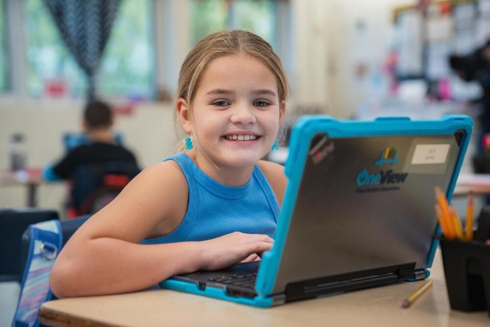Elementary school student smiles as she works on her laptop in the classroom