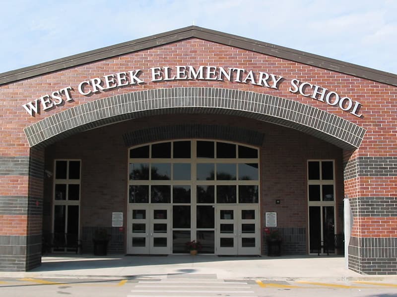 The entrance to West Creek Elementary School, a brick building with large glass doors.