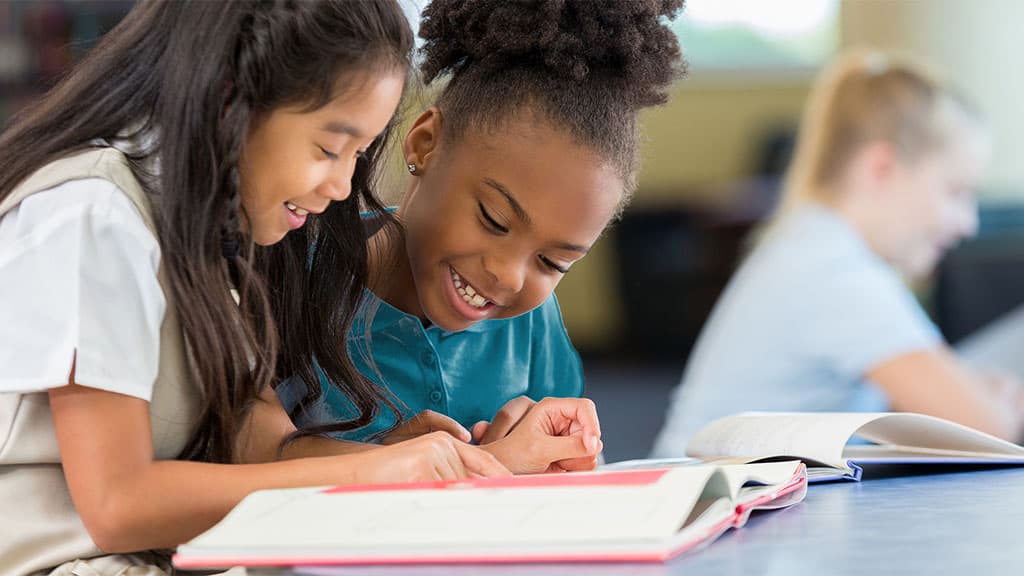 Smiling and cheerful schoolgirls reading a book