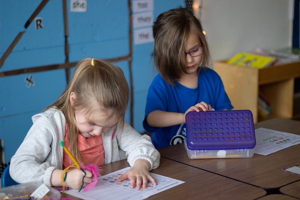 Two girls work at their desks on worksheets.