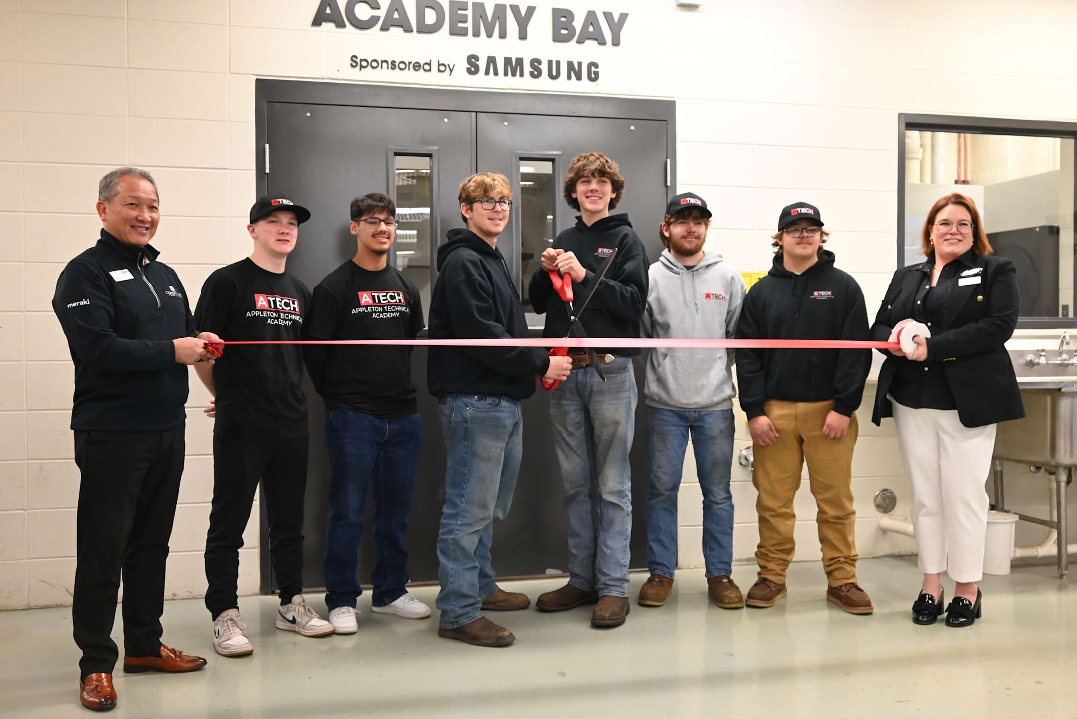 A group of people, some wearing uniforms, are gathered in front of a sign that says %22ACADEMY BAY%22 and is sponsored by Samsung.