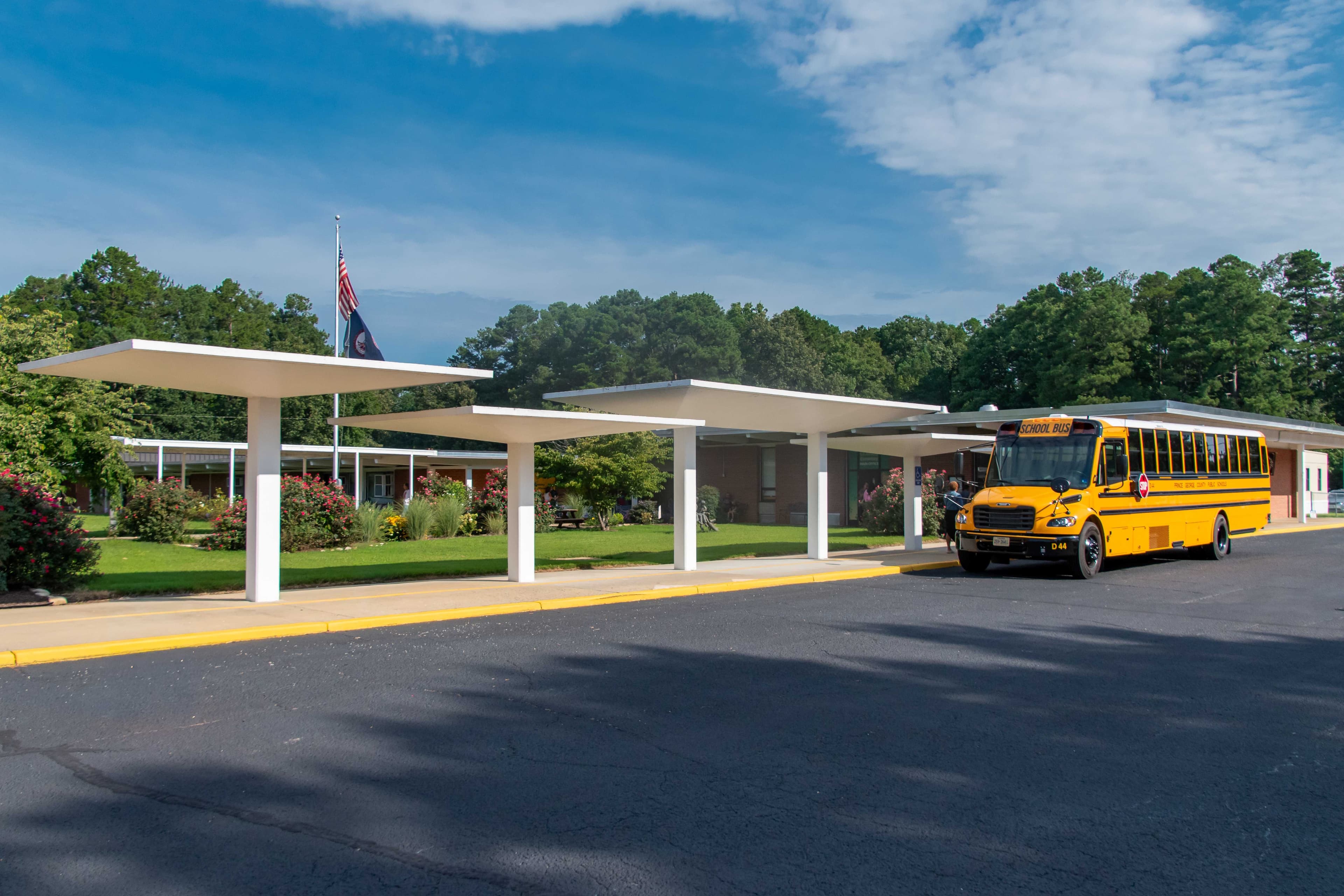 A yellow school bus is parked at a covered bus stop outside Beazley Elementary.