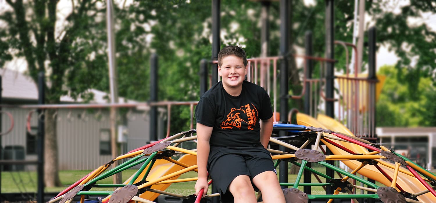 A person sits outdoors, smiling, with a blurred background of trees.