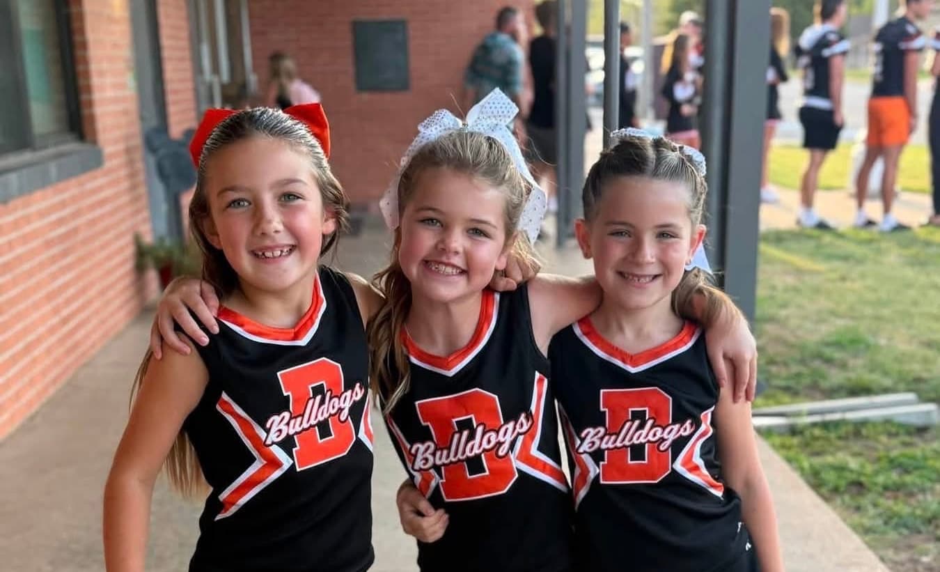 Three young girls in matching black and red outfits smile for the camera.