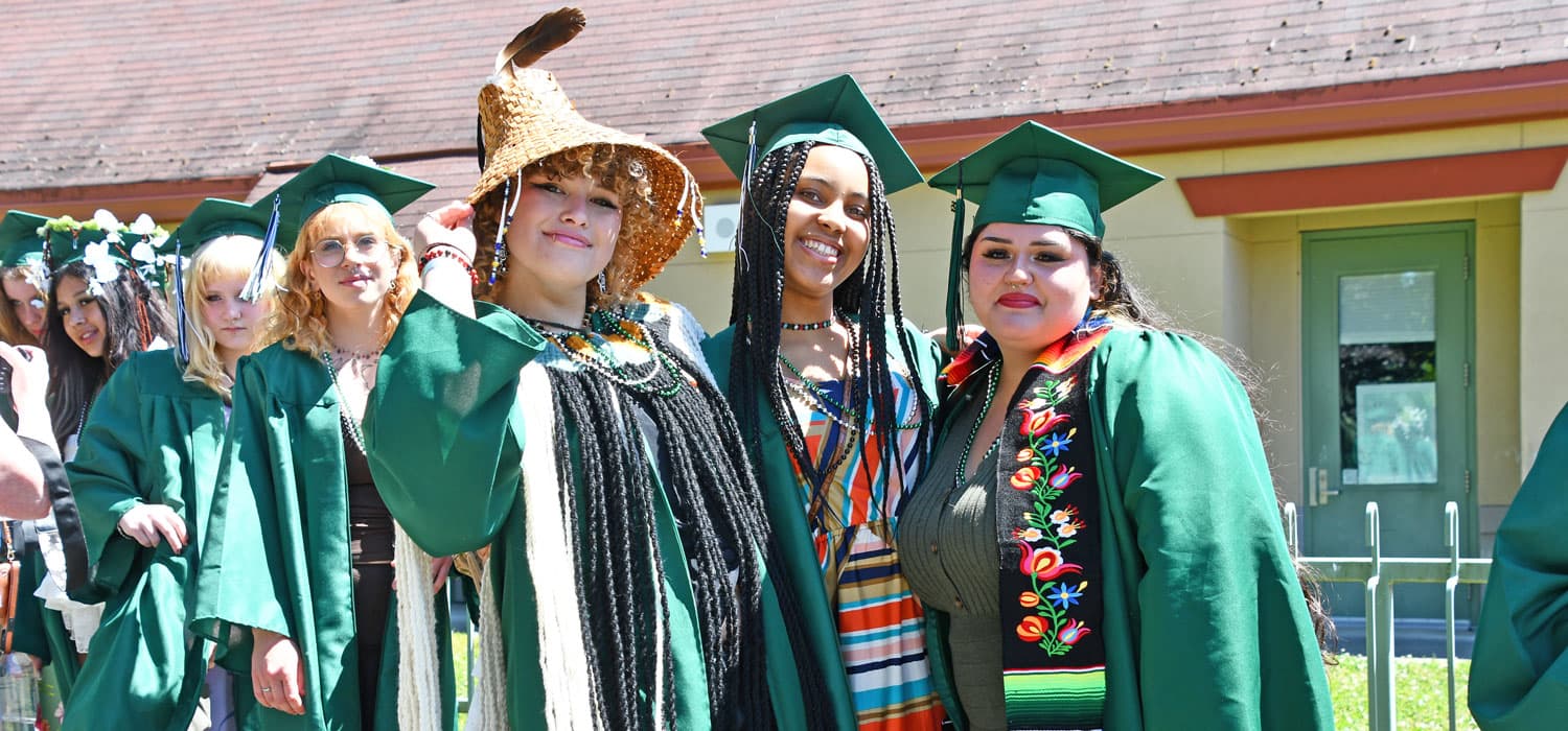 Graduates in green gowns and caps walk together, smiling.