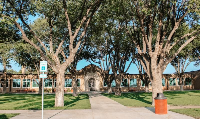 A building with a central arched entrance is framed by large trees.