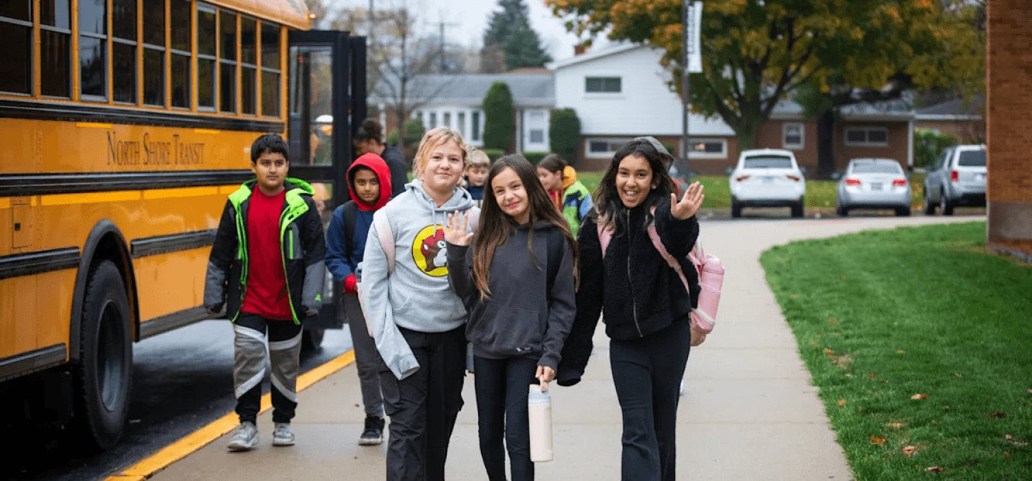 students standing outside in front of a parked school bus, smiling