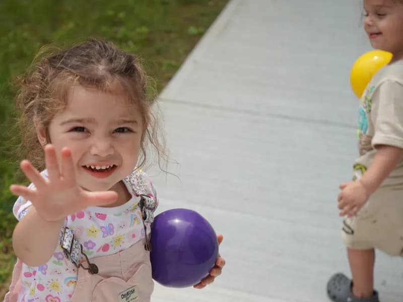 Smiling toddler holding purple ball outdoors
