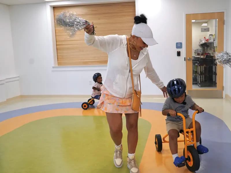 Woman cheering child riding tricycle indoors