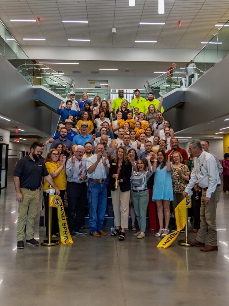 Staff and community members celebrate at a ribbon-cutting ceremony on a modern school staircase with Sand Springs Middle School banners.