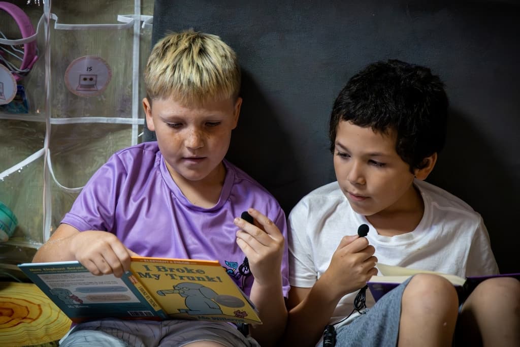 Two elementary students holding microphones and reading "I Broke My Trunk" by Mo Willems.