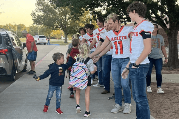 A group of young athletes in white jerseys with 'Jackets' and numbers on them high-five children as they walk by.