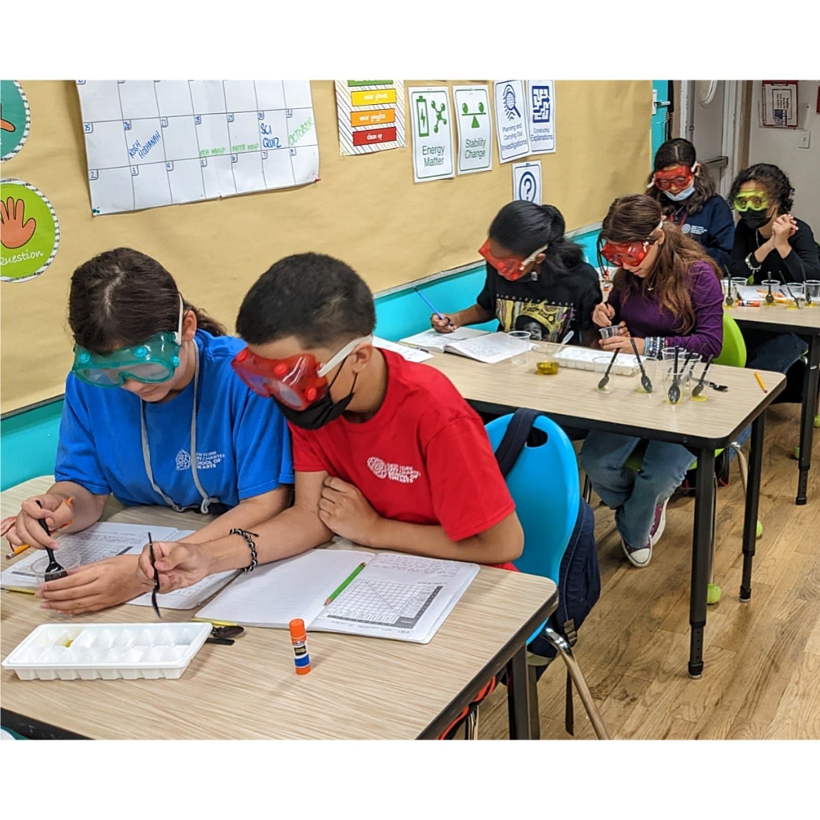 Children in a science classroom wearing protective goggles and working on experiments at their desks.