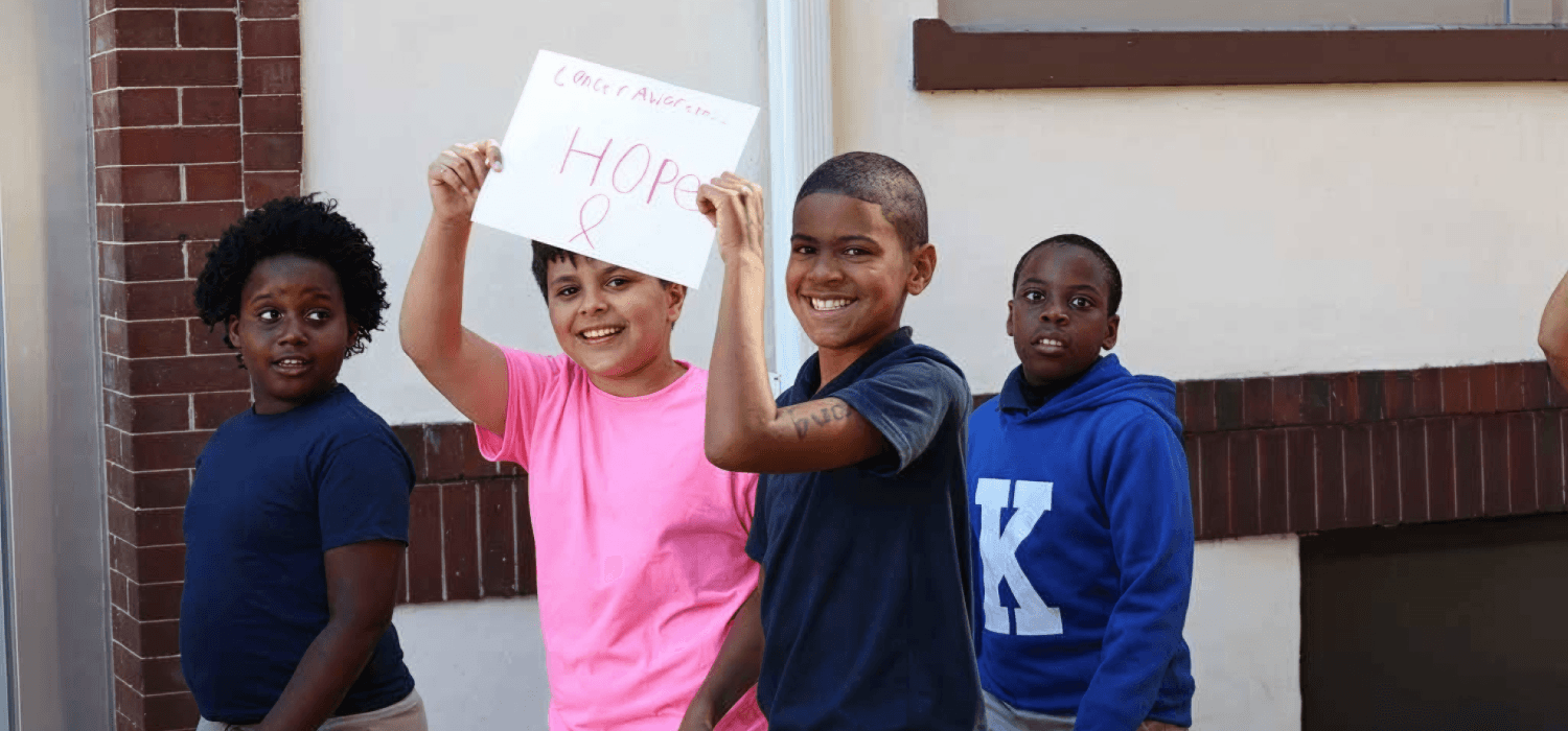 Four children stand together, with two holding up a sign.
