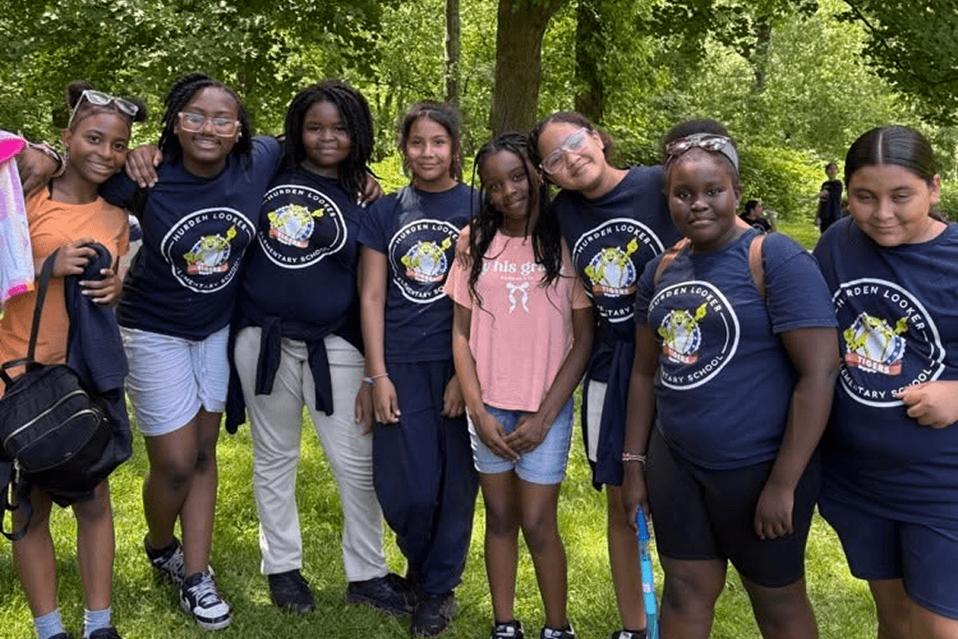 A group of young people in matching t-shirts stand together outdoors, smiling.
