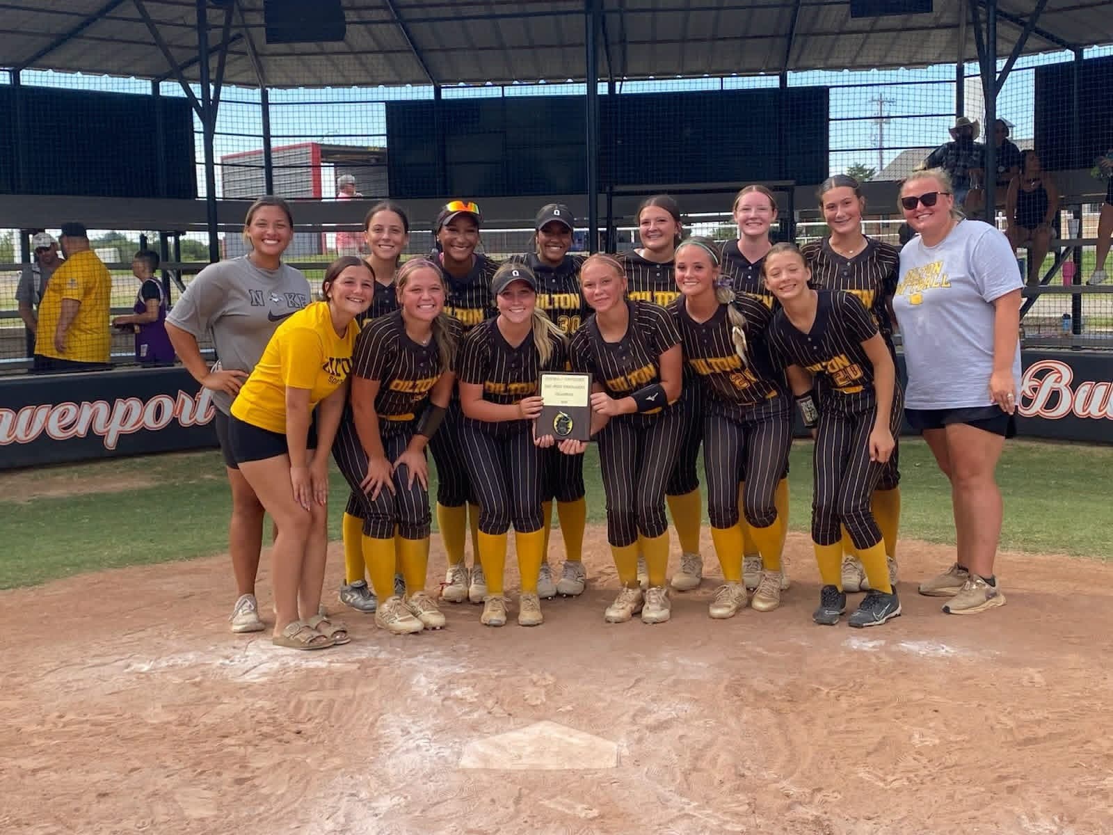 A youth softball team stands proudly on the pitcher's mound, holding a trophy after a game.
