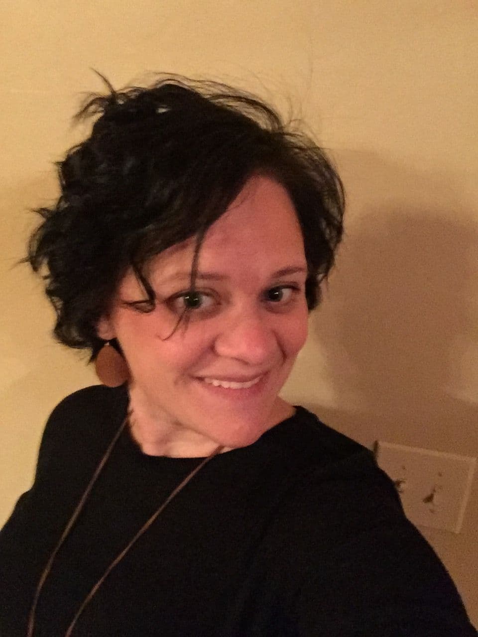 A woman with dark, curly hair smiles at the camera.