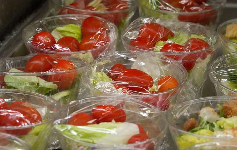 Salad prepared in individual containers and covered in plastic wrap.
