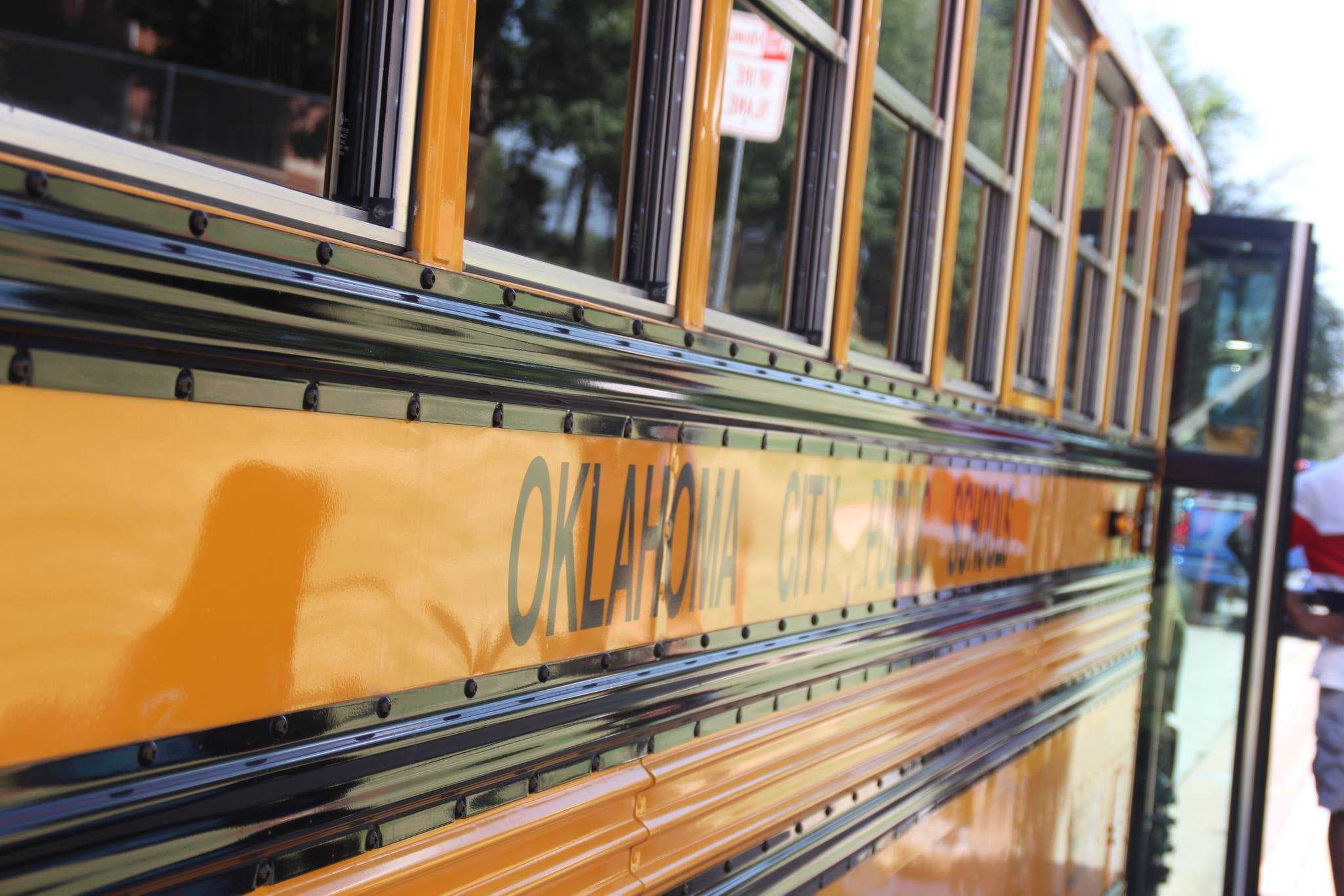 A yellow school bus with "Oklahoma City Public Schools" written on its side is parked outdoors with a person standing near its open door in the background.