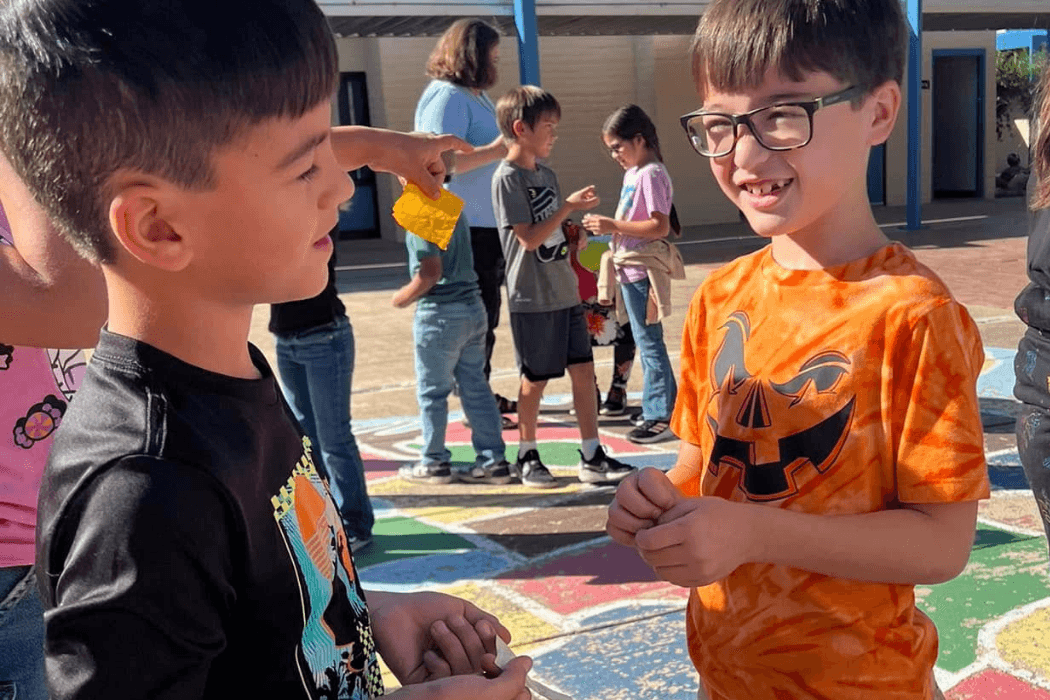Two young boys converse outdoors at school.