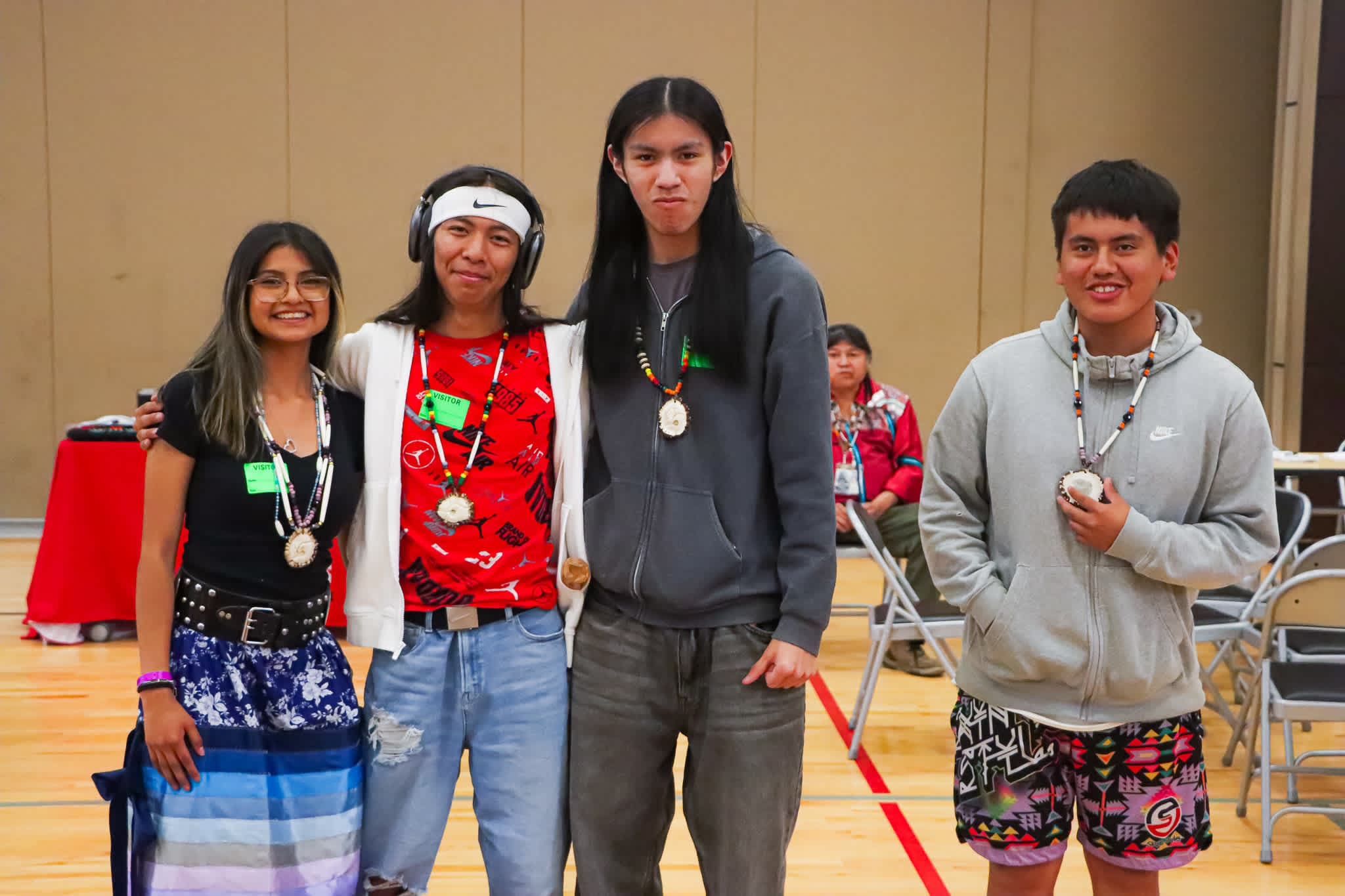 A group of young people, dressed in casual attire, are standing together in what appears to be an indoor setting with a plain background.