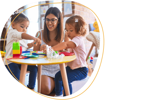 Young beautiful teacher and toddlers playing meals using plastic food and cutlery toy at kindergarten.