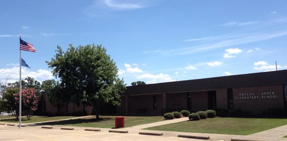 Poteau Upper Elementary School facade with American and Oklahoma flags, surrounded by trees and blue sky.