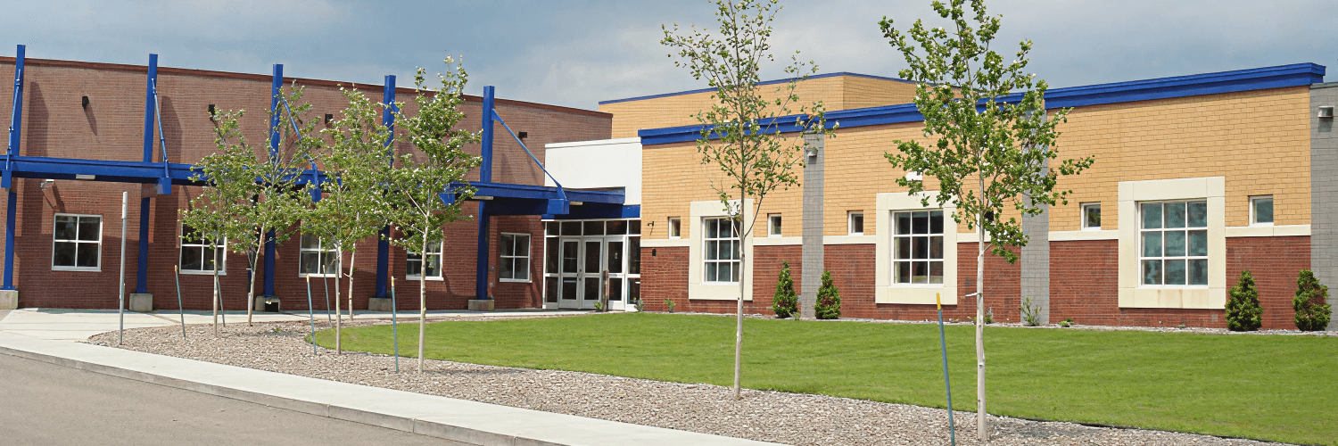 A modern building with brick and tan sections, featuring blue accents and trees.
