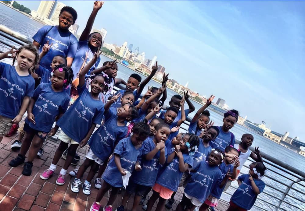 A group of children in blue shirts joyfully raising their hands, embodying a mission to serve children in their community.