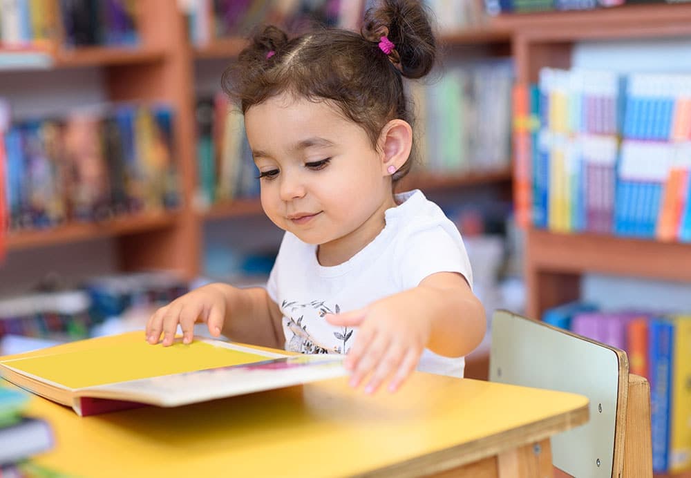 A young girl immersed in a book, representing the value of early learning in fostering academic success.