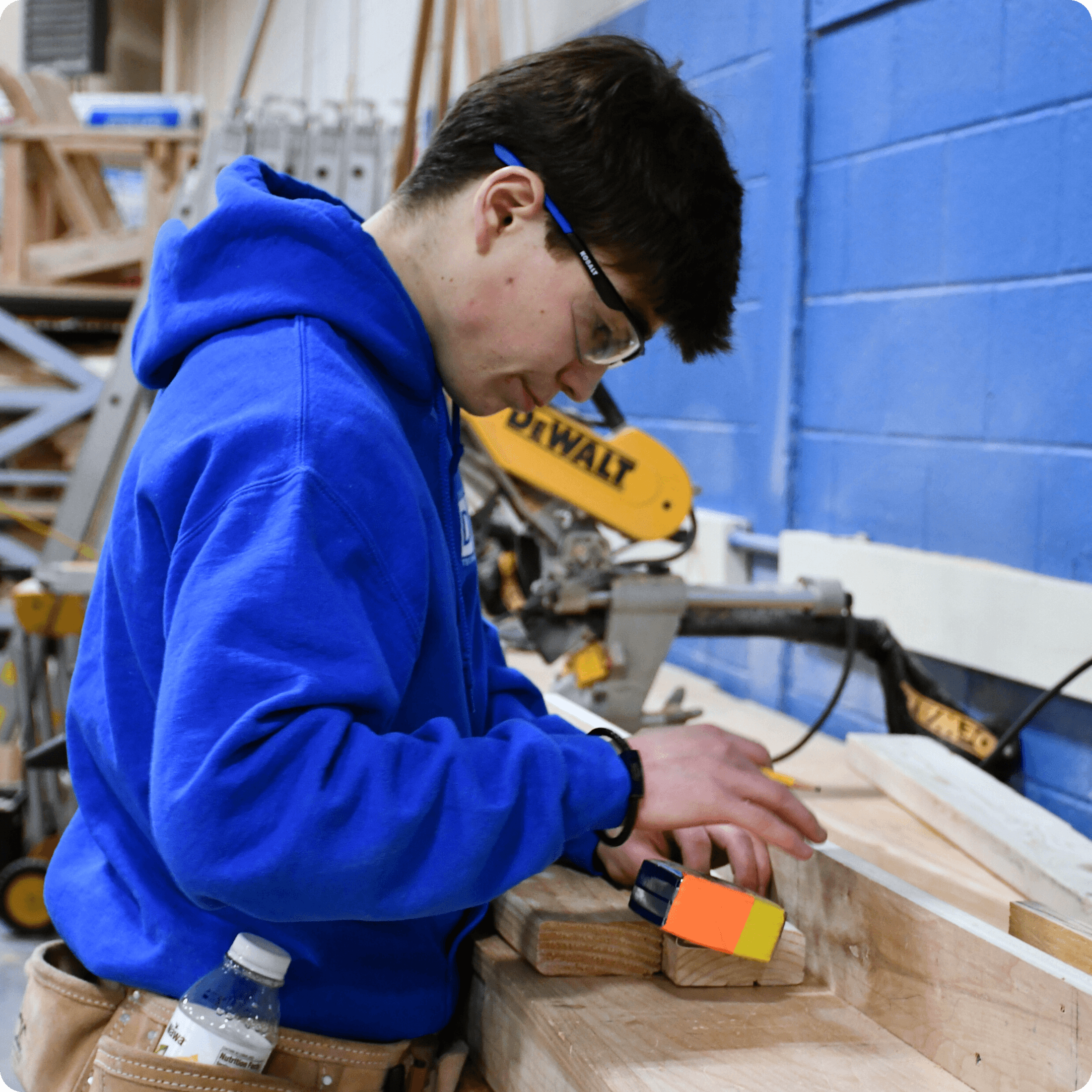 Student measures wood pieces at a workbench in the carpentry lab.