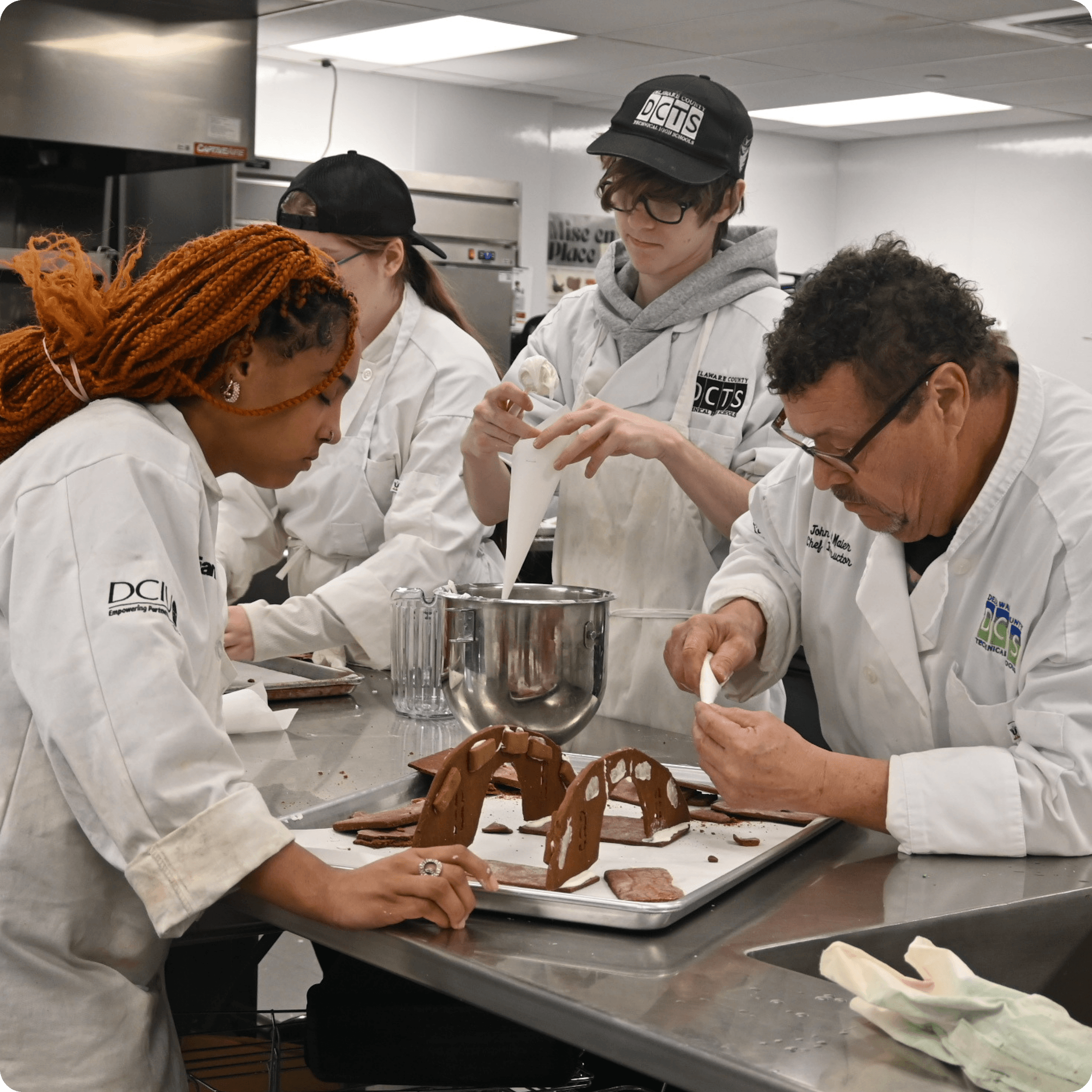 Culinary students and instructor decorate gingerbread structures in the kitchen lab.