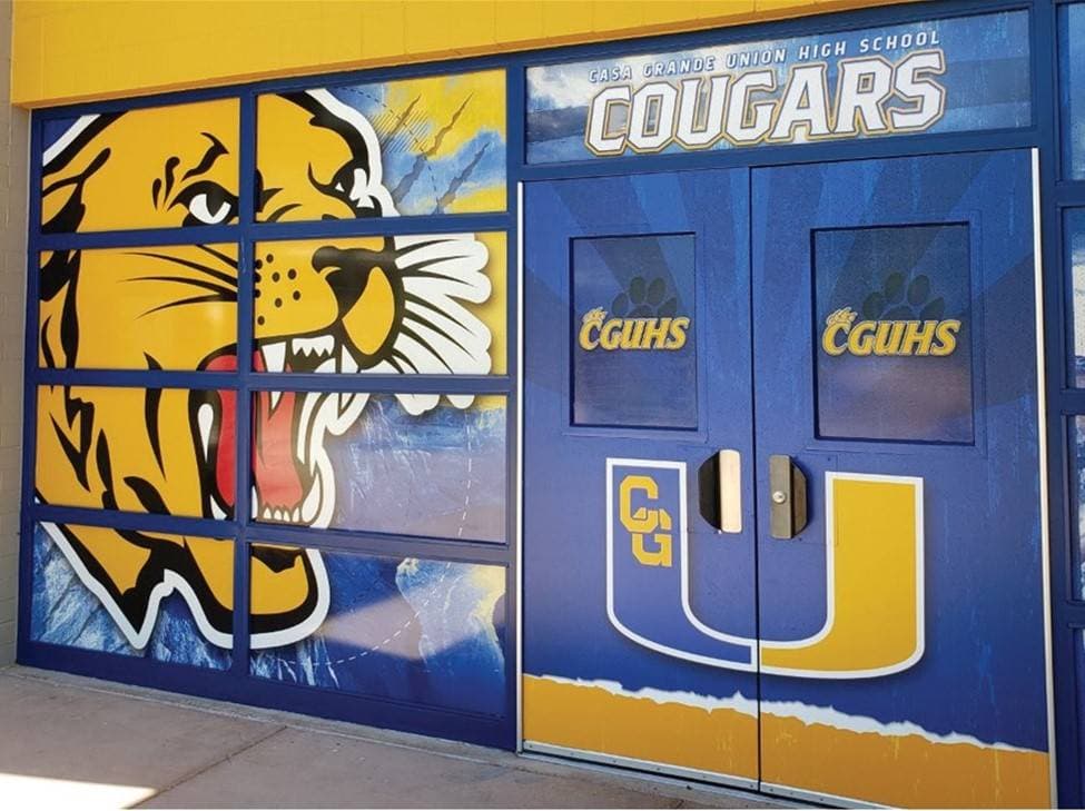 A vibrant mural featuring a roaring cougar and the word 'COUGARS' on a blue and yellow background, displayed on a set of double doors.