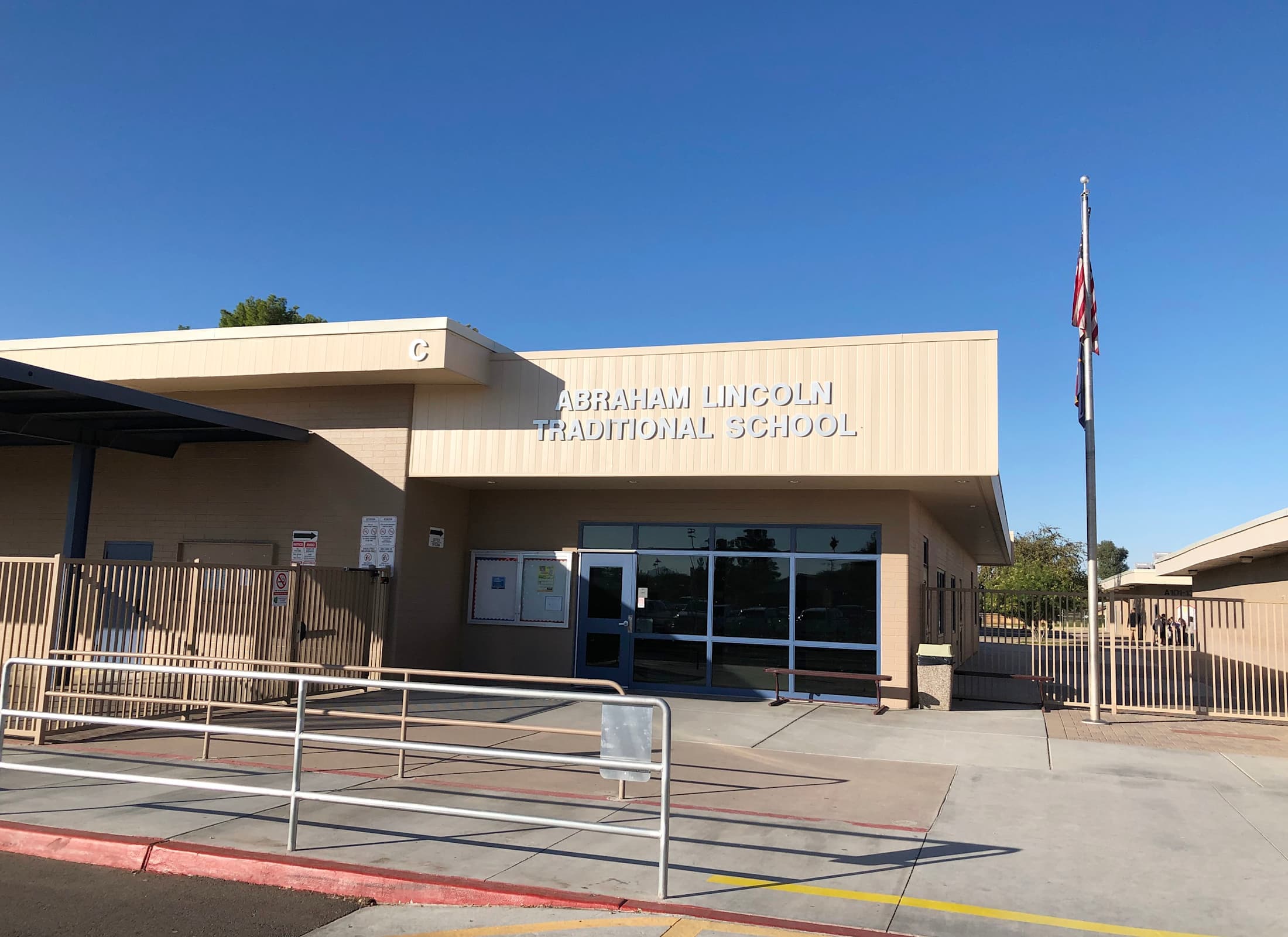 The image shows the exterior of a school building called %22Abraham Lincoln Traditional School%22, with a flag pole and ramp leading to the entrance.
