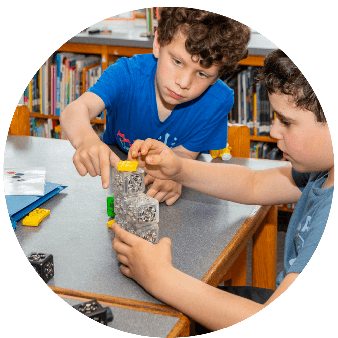 Two young boys collaborate on a building project at a table.