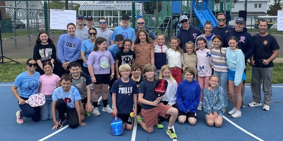 A large group of people, including children and adults, pose for a photo on a blue court.