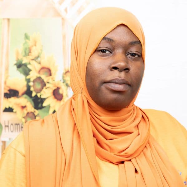 Woman wearing an orange hijab with sunflowers in the background.
