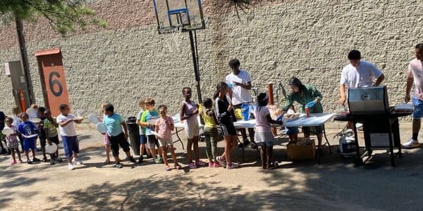 Children lined up outdoors for a barbecue or food event.
