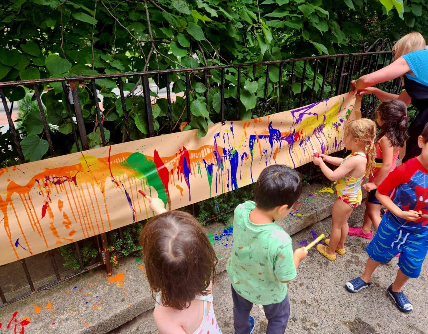 A group of children painting on a long piece of wood.