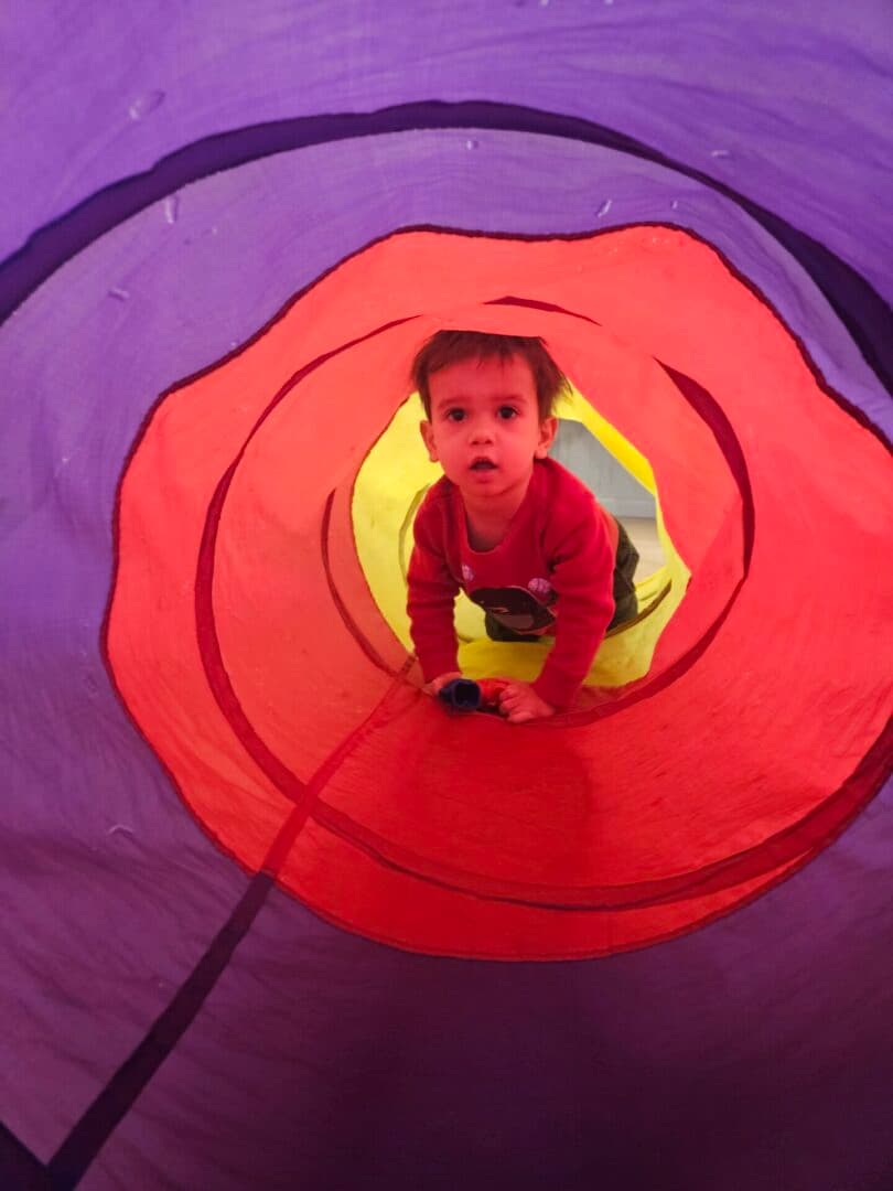 A toddler is inside of an indoor play tunnel.