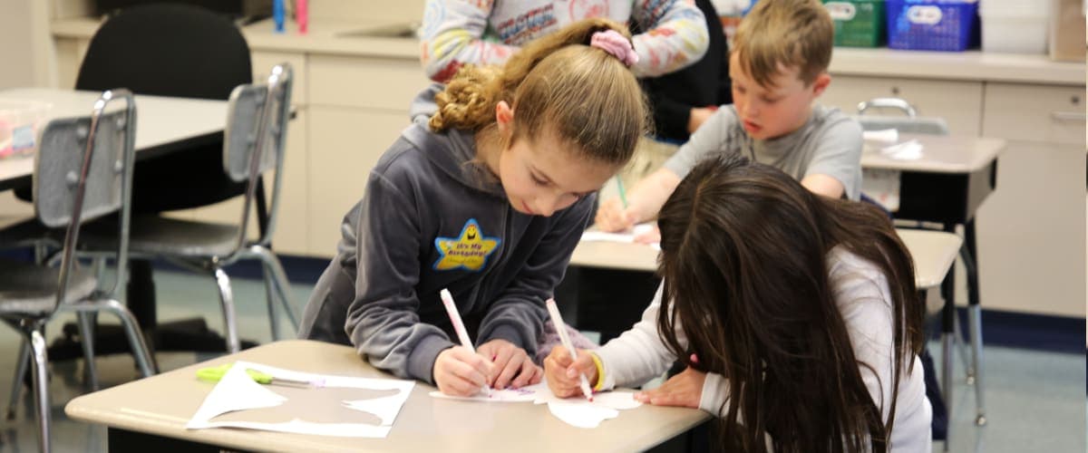 two female students sharing a desk and drawing a picture of a butterfly