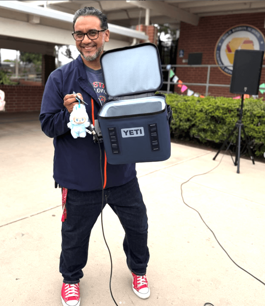Principal Eric Barrientos stands with a Yeti cooler and a small labubu