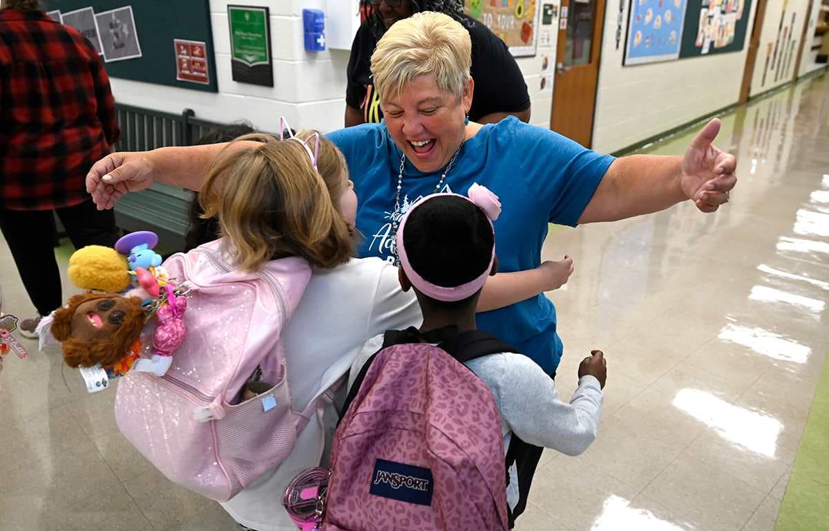 A teacher hugs two students