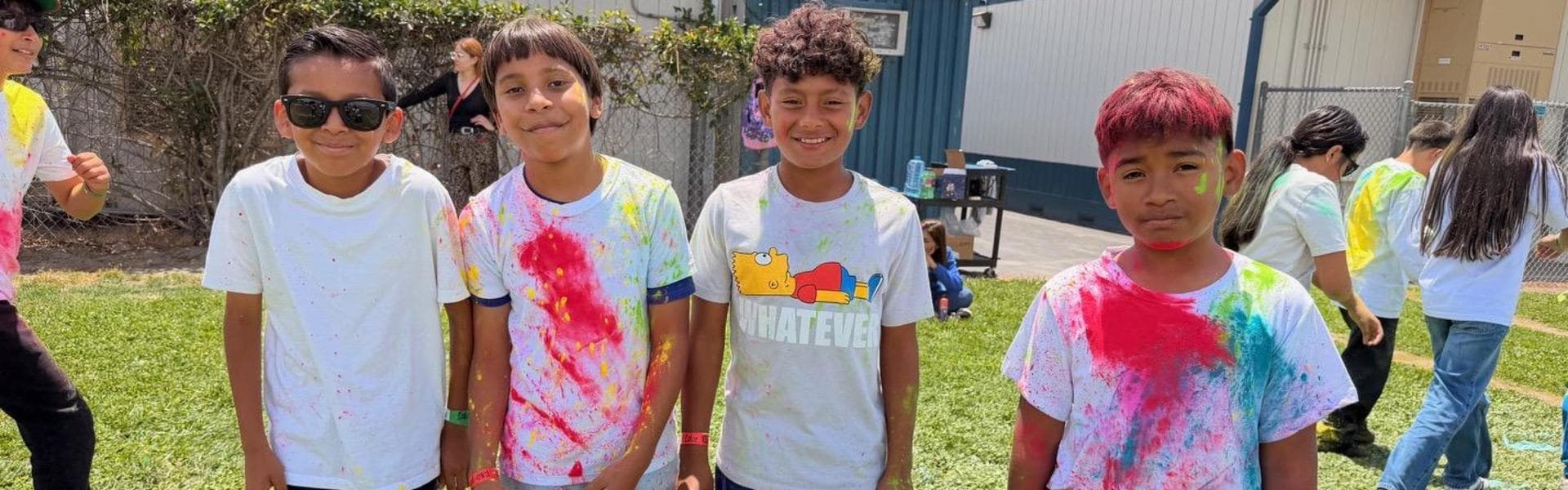 Four boys standing together covered in colorful powder on their clothes.