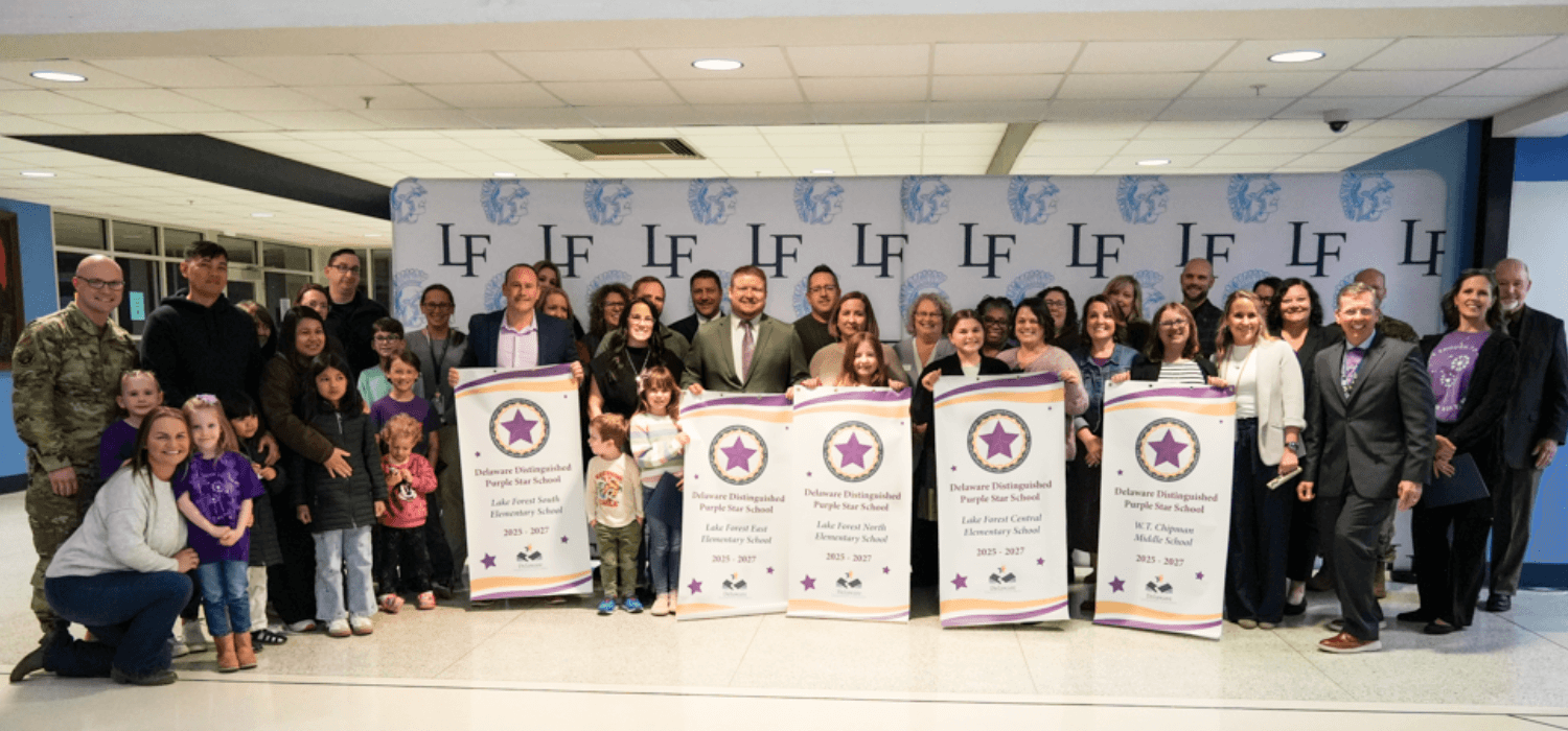 A large group of people pose together indoors, holding signs.