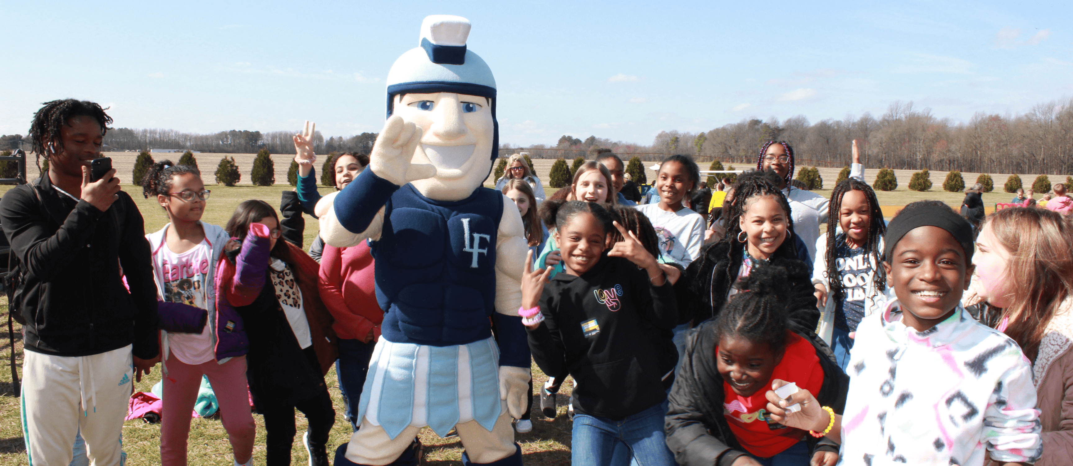 A mascot poses with a group of children outdoors on a sunny day.