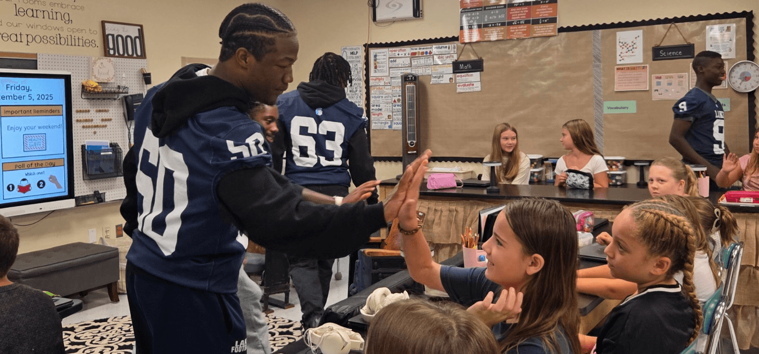 Students and a teacher interact in a classroom setting.