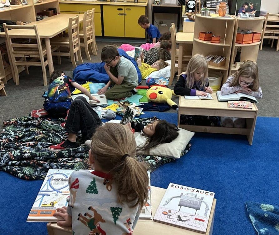 Students reading books in their classroom snuggled with pillows and blankets.