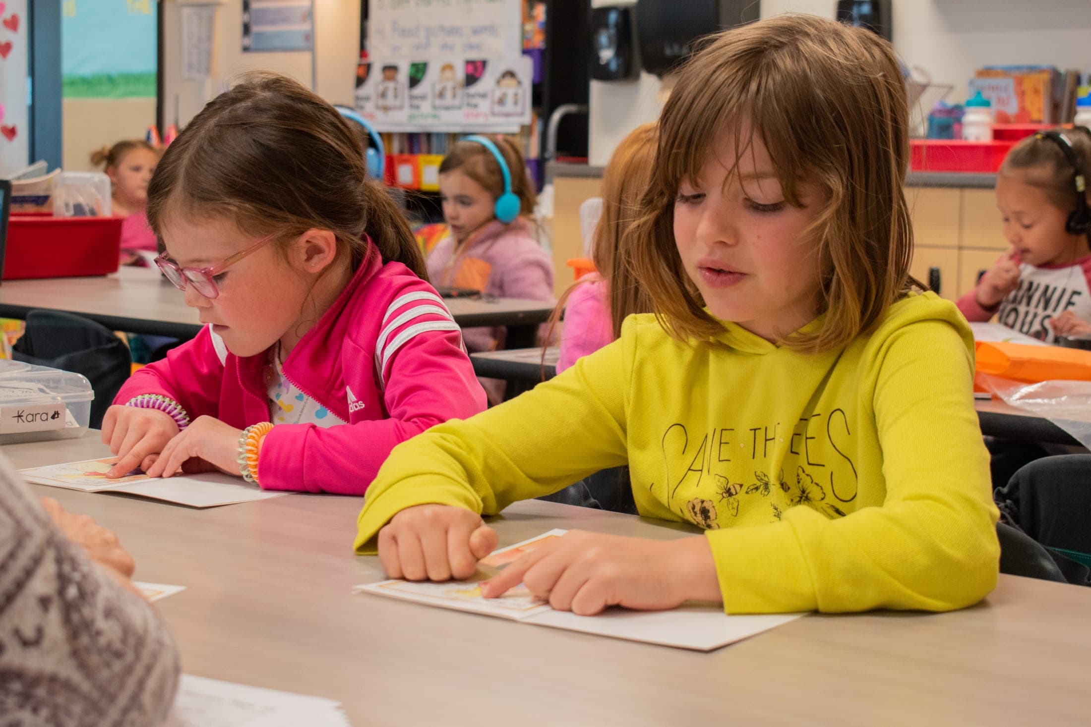 two girls sitting at desks and writing on paper