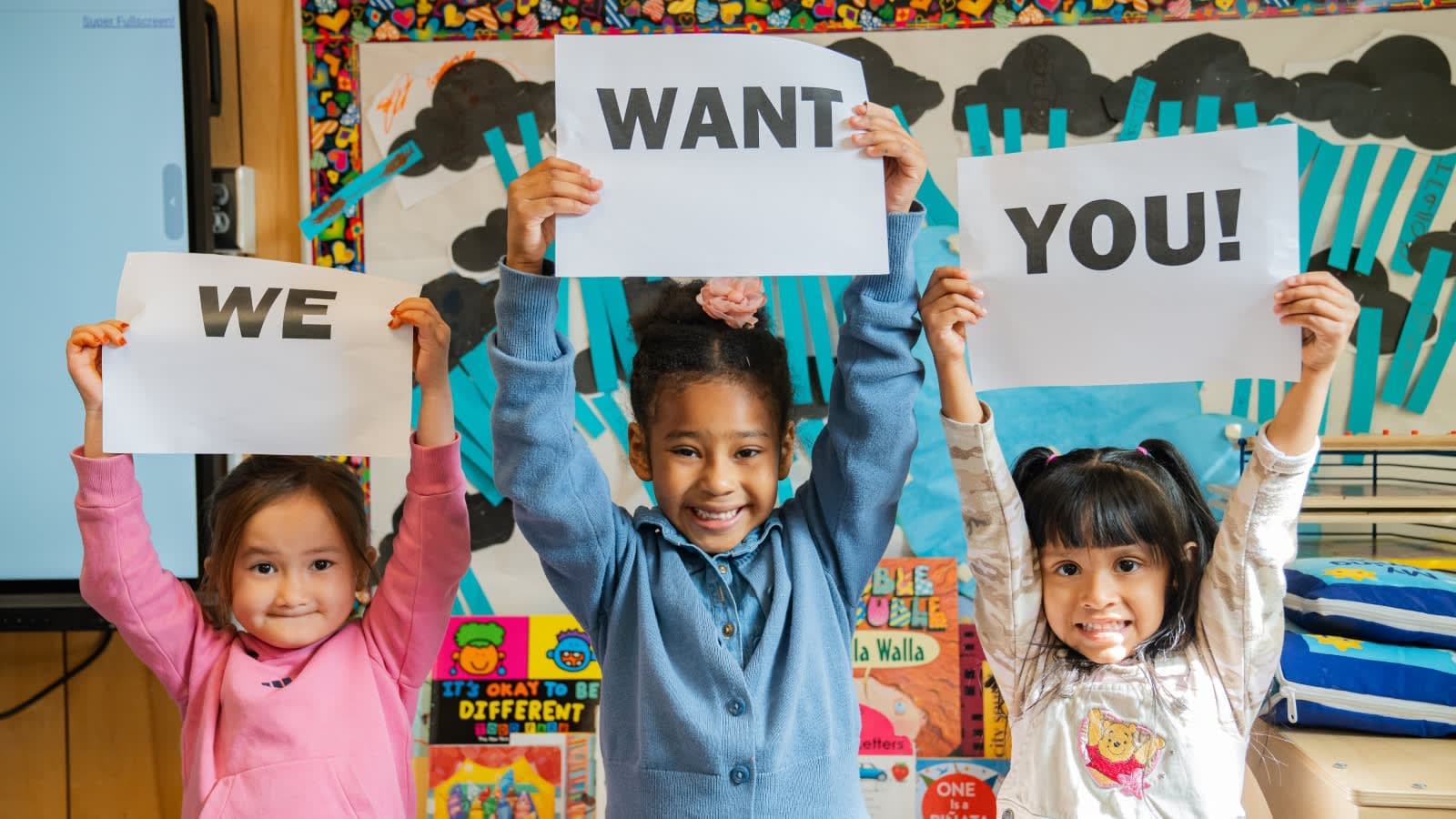 Young students holding signs that read We Want You